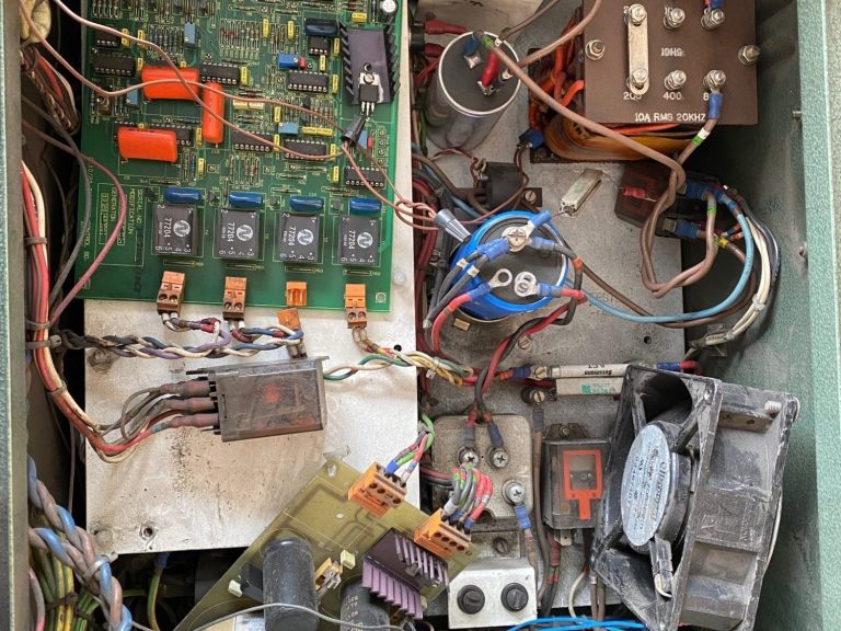 Detailed view of the inside of a faulty corona power supply, showing circuit boards with various wires, components, and a fan.